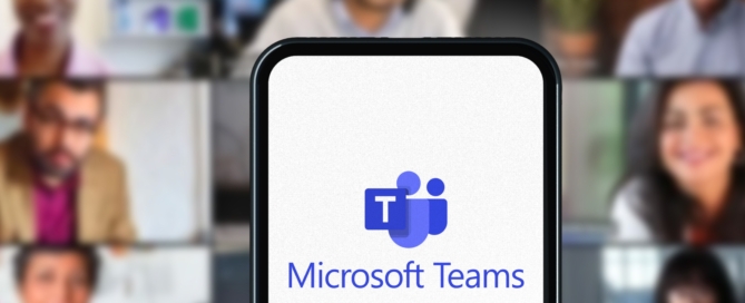 A phone showing the Microsoft Teams Logo is set in front of a background of individuals all on a video call.